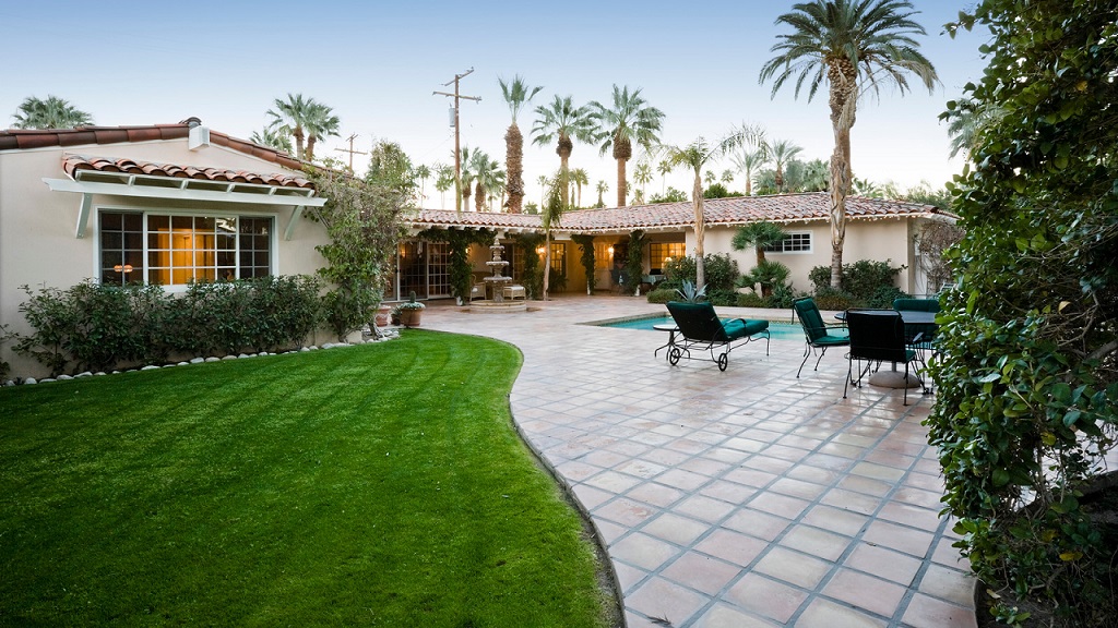 Landscaped backyard with palm trees, manicured lawn and a paved poolside patio